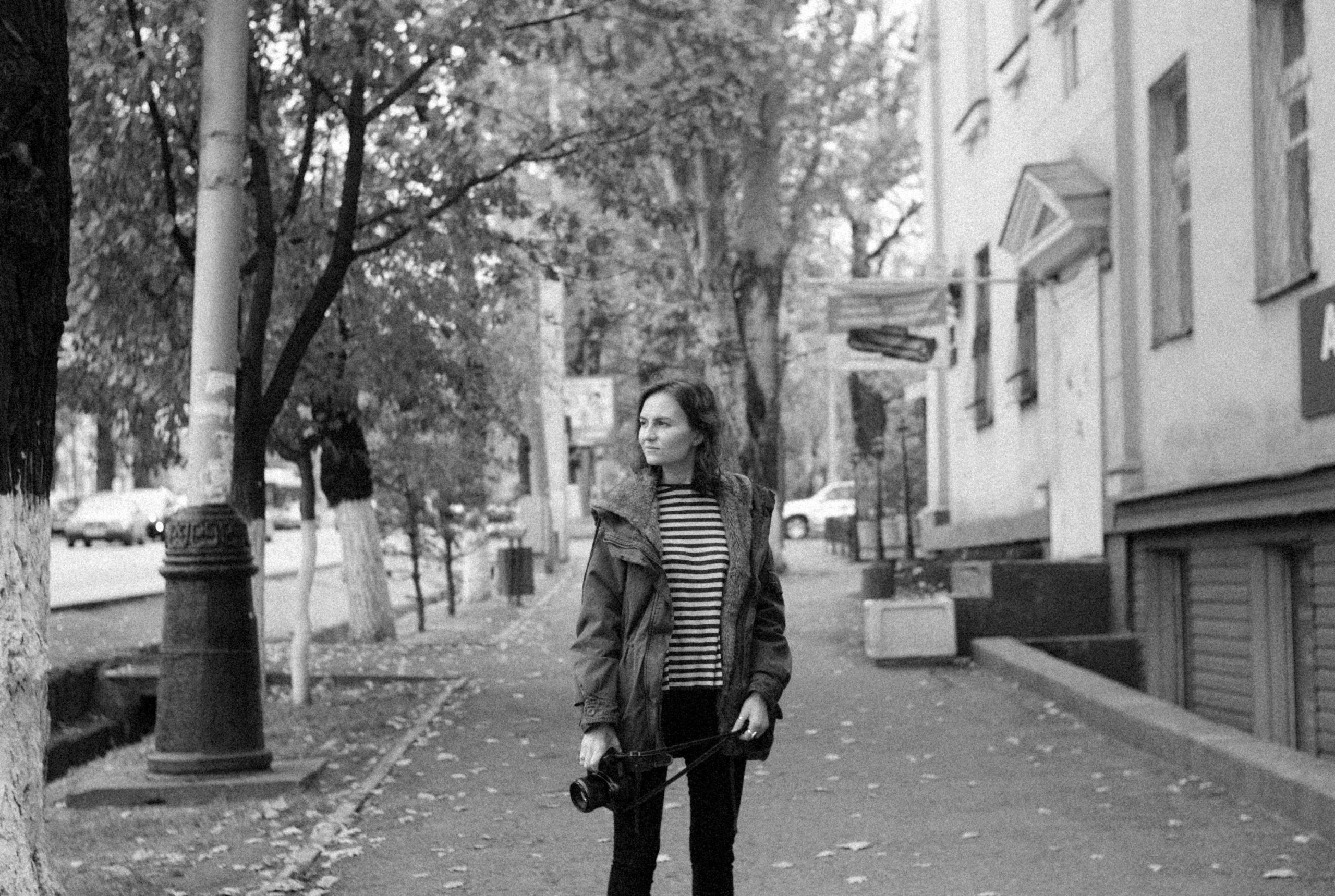 Black and white image of a woman with a camera on a city street.