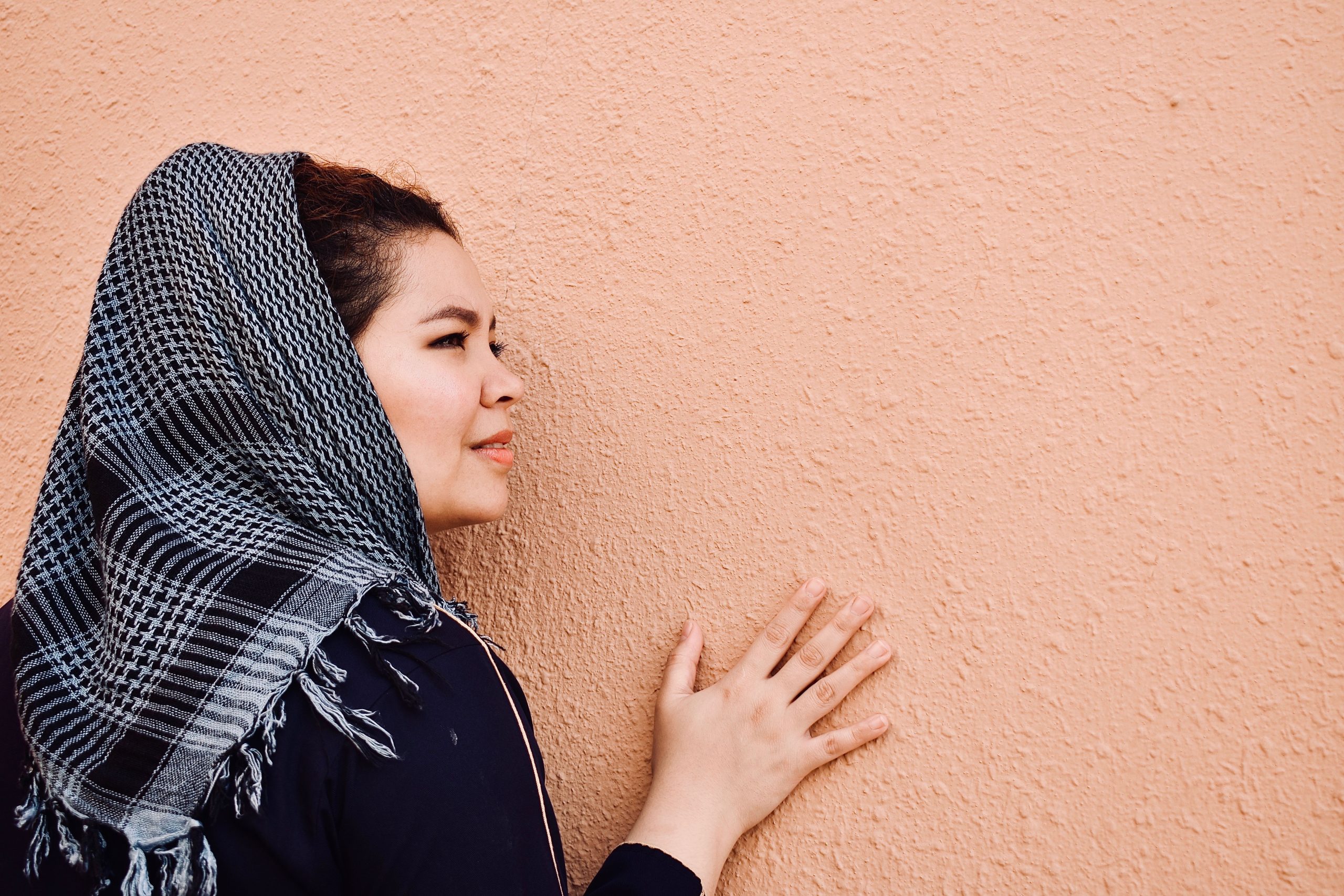 A woman in a headscarf touching a textured wall in Saudi Arabia.