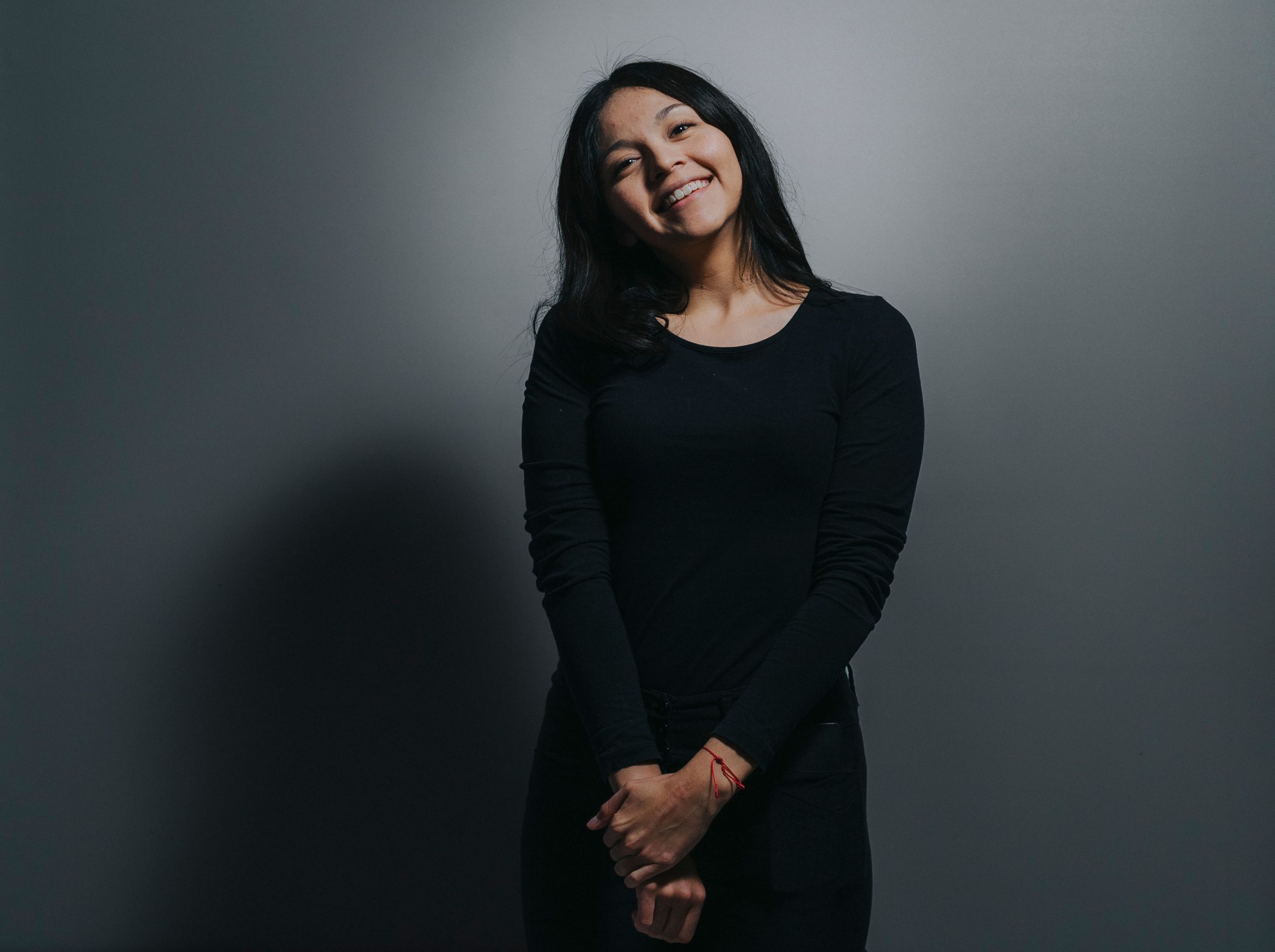 Simple portrait of a woman in black clothing smiling against a gray background.