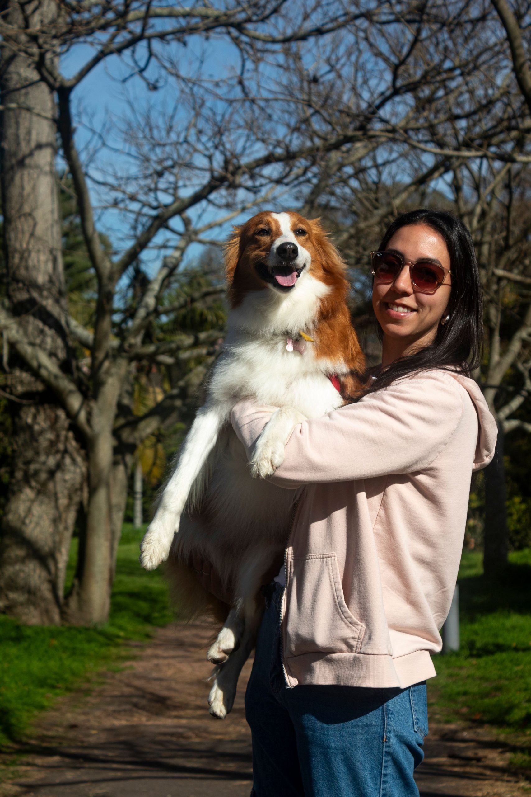 A cheerful woman holds a happy dog in a sunlit park in Montevideo, Uruguay.