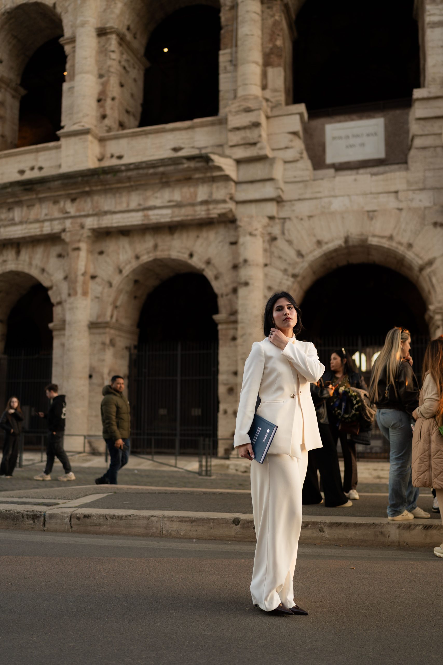 Woman in white suit stands confidently near the historic Colosseum in Rome, Italy.