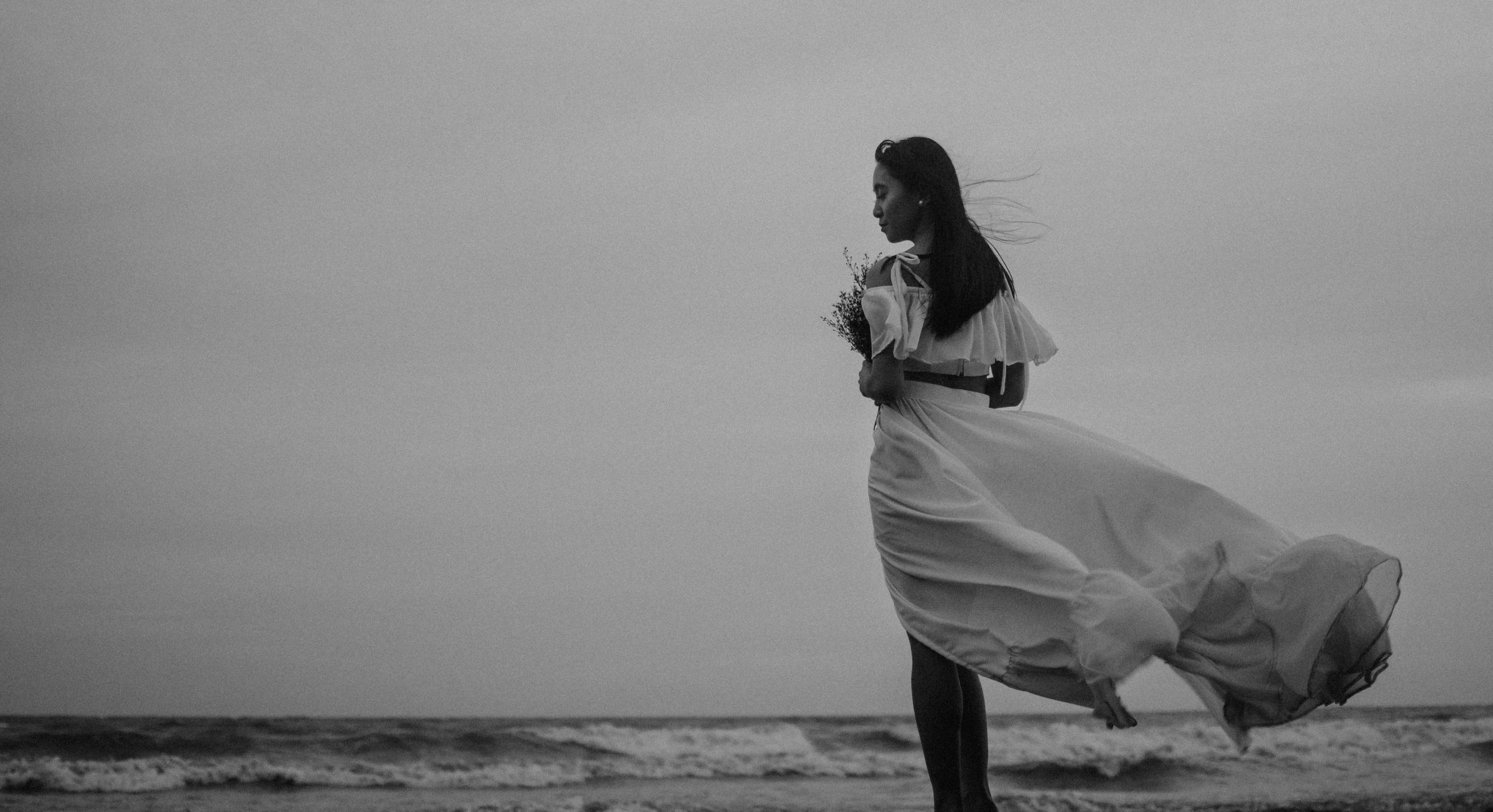Elegant silhouette of a woman in a flowing dress by the ocean at dusk.