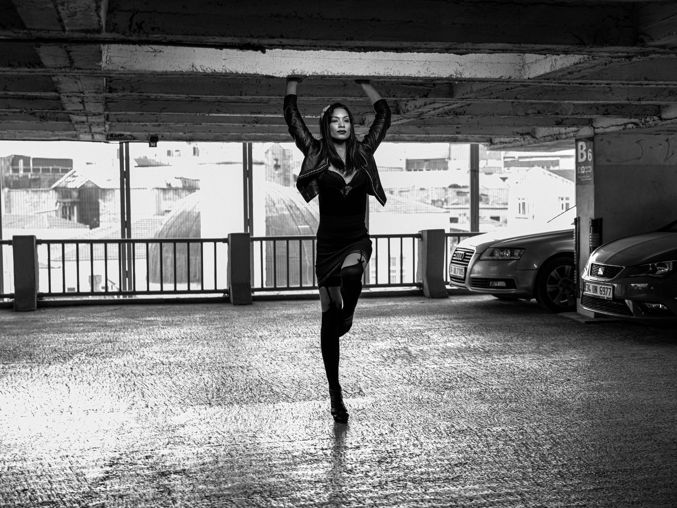 Black and white photo of a woman posing with arms raised in a car park.